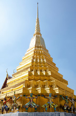 Fototapeta na wymiar Bangkok, Thailand - Golden statues are holding a golden tiered building over their head. The tiered building terminates in a spire.