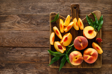 Ripe peaches with leaves in basket on wooden table, top view