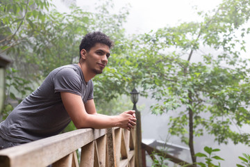 Hispanic traveler man lying on a balcony of a natural park surrounded by trees and fog enjoying -...