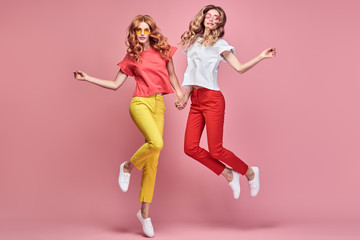 Naklejka na ściany i meble Fashion. Two Inspired woman laughing dance. Shapely joyful friend Having Fun, Stylish fashionable summer outfit. Carefree Girl friends with curly hair jump dancing in Studio, happy positive emotion