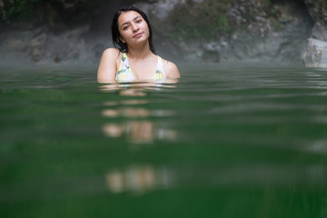 Young Hispanic woman enjoying hot springs - Latina traveler in the middle of volcanic rocks and takes a bath in the natural thermal waters of spa - Guatemala woman in swimsuit