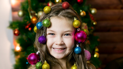 Fototapeta na wymiar Little girl with garlands holiday balls woven into her hair with Christmas decorations. Girl with Christmas decorations on her head.