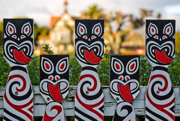 New Zealand, Rotorua. Fence painted with Maori warrior faces surrounds the Rotorua Museum seen in background.