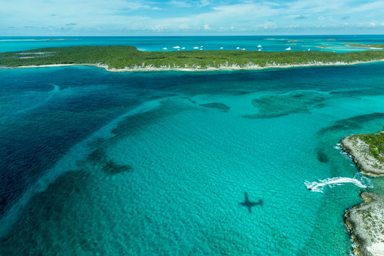 Aerial Photo Looking Down At The Airplane's Shadow, A Jet Ski And Clear Tropical Water And Islands In The Exuma Chain Of Islands The Bahamas Near Staniel Cay.