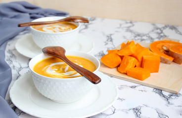 Two bowls of pumpkin soup on white background with gray fabric and slices of butternut squash,top view,vegetarian food