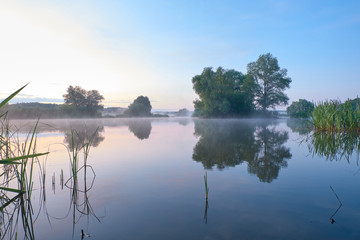 Naklejka na ściany i meble Foggy morning. Dawn outside the city. It will be a warm day. Morning fog on the lake