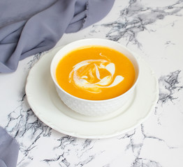 Two bowls of pumpkin soup on white background with gray fabric and slices of butternut squash,top view,vegetarian food