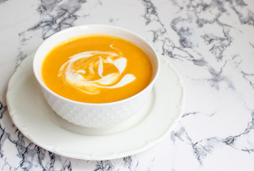 Two bowls of pumpkin soup on white background with gray fabric and slices of butternut squash,top view,vegetarian food