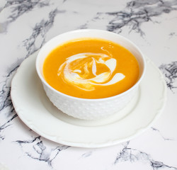 Two bowls of pumpkin soup on white background with gray fabric and slices of butternut squash,top view,vegetarian food