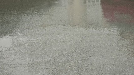Rain drops are dripping on the wet asphalt. Feet walk on the wet road during rain in summer rainy day. Girl and guy legs walking on grey wet from rain road, side view.