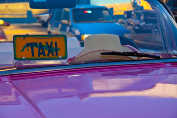 Havana, Cuba, colorful image of a bright pink taxi hood and windshield with a straw cowboy hat in the window