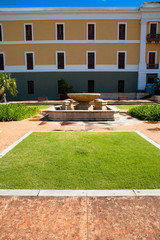 Obraz premium San Juan, Puerto Rico - A hotel fountain in a courtyard is sitting with no water in it. A patch of grass can be seen in the foreground bordered by walkways.