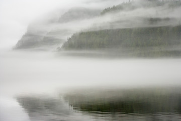 Canada, British Columbia, Calvert Island. Mist and fog shroud water and forested island.  - obrazy, fototapety, plakaty