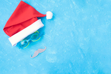 Hat of Santa Claus with goggles for swimming and a mustache. Christmas vacation, sandals and swimming glasses by water, slippers and pool goggles near swimming pool