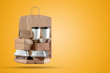 Pizza boxes and food delivery paper bag with a disposable cup of coffee and a wok box on a yellow background. Home delivery of goods from a store or restaurant. Copy space