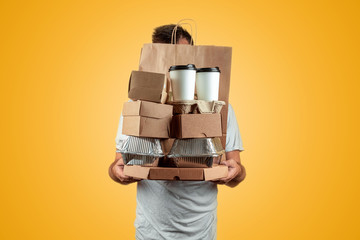 Man in a bright T-shirt giving a fast food order isolated on a yellow background. Male worker courier hold a packet of food. Home delivery of goods from a store or restaurant. Copy space