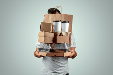 Man in a bright T-shirt giving a fast food order isolated on a blue background. Male courier worker is holding food. Home delivery of goods from a store or restaurant. Copy space