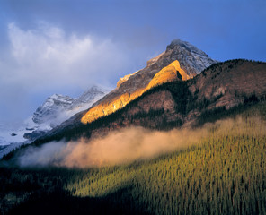 Canada, Alberta, Banff NP. Sunrise strikes the flank of the Canadian Rockies as clouds swirl in...