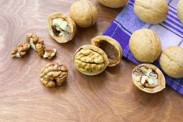 Whole walnuts and walnut kernel halves without shell on a dark wooden table and checkered towel, close up. Seeds of the common walnut tree Juglans regia. Macro food photo close up view.