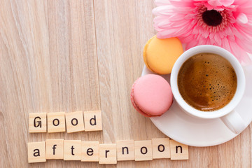 Good afternoon message coffee break concept  white cup of frothy espresso coffee with colourful French macaroons on wooden background, space for text.