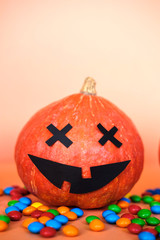 Halloween pumpkin jack o lantern decor with funny face and colorful candy on orange background. Trick or treat. Happy Halloween celebration concept. Copy space