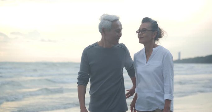 Asian senior couple walking and talking on beautiful tropical beach in slow motion.