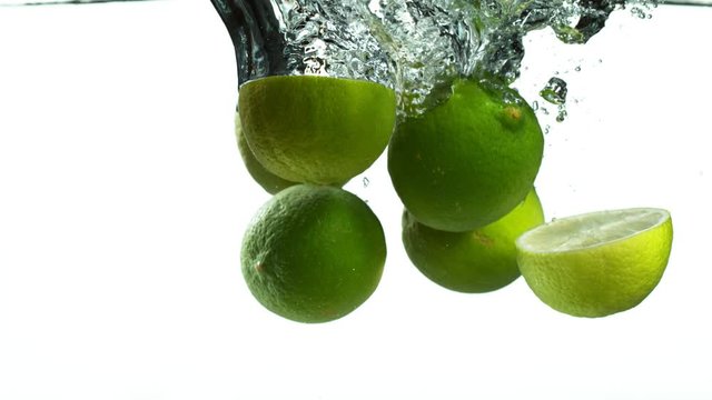 Super slow motion of falling lime pieces into splashing water isolated on white background. Filmed on high speed cinema camera, 1000 fps.
