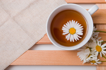 cup with chamomile tea on a beige fabric with daisies on a wooden tray white background isolation top view copy space