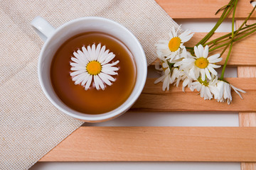 Obraz na płótnie Canvas cup with chamomile tea on a beige fabric with daisies on a wooden tray white background isolation top view copy space