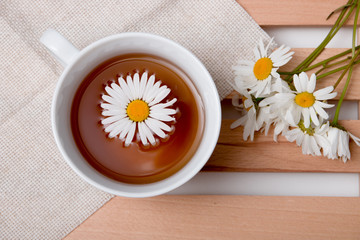 cup with chamomile tea on a beige fabric with daisies on a wooden tray white background isolation...