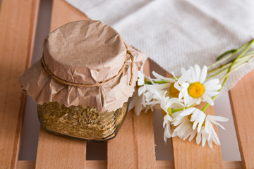 a jar of herbal tea stands on a wooden tray of rekk with a daisy flower and a beige coarse cloth copy space top view