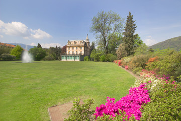 spring landscape with pink flowers and beautiful villa house with fountain in bright day blue sky background.
