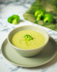 Fresh Broccoli cream soup on two gray ceramic bowl on plate with spoon on marble background,vegetarian food,healthy concept