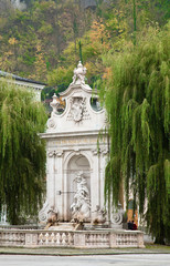 Obraz premium Salzburg, Salzburg, Austria - A large stone, shrine with a statue in an outdoor setting. It is surrounded by trees and two visitors sit off to the side.