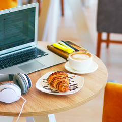 coffe, laptop and croissants to show a business breakfast on the office table in morning