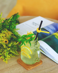 Lemon water, lemonade in mugs with handles, mason jar on a white wooden table. Yellow flowers and journal in the background.