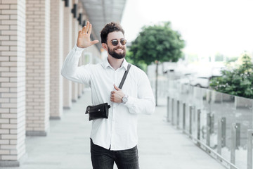 Fototapeta premium A bearded, happy, smiling, stylish man greetings with friends on the streets of the city near modern office centre