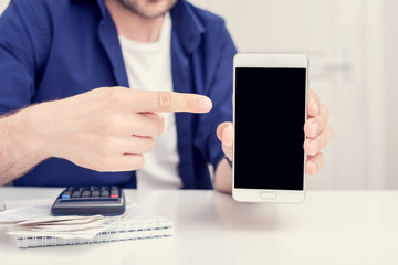 Guy calculates family budget, he pays for the expenses with his smartphone, shows screen smartphone, cropped image, close up, toned