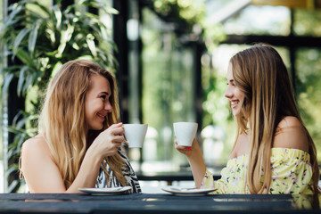 Pretty, gorgeous mother with her young daughter drinking latte in modern cafe terrace. Weekend time.