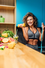 Portrait of beautiful cheerful girl holding in hand measure and dumbbells, dietitian and healthy...