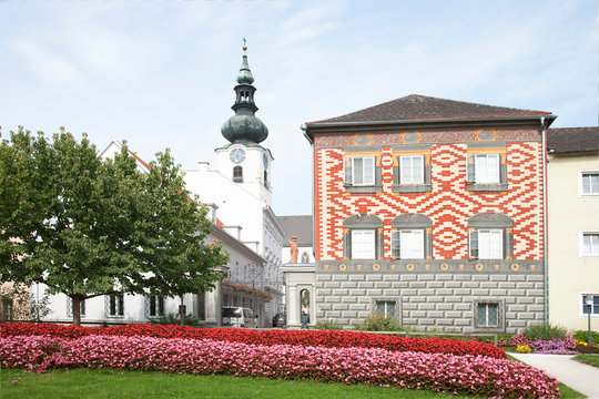 Wels, Upper Austria, Austria - Rows of red and pink flowers border a lawn in front of a building. In the background is a clock tower with a spire. - Powered by Adobe