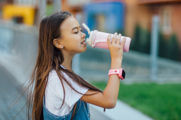 Portrait of young small girl drinking water from thermos, on hands smart watches.