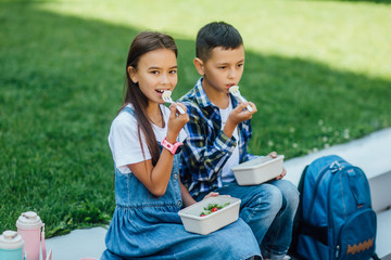 Portrait of of two junior children in a school time during lunch break, holding lunch boxes with...