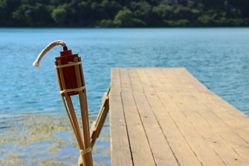 Close up tiki torch filled with citronella liquid  for mosquitoes at a pier at lakeside, blurred...