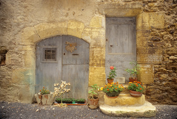 Fototapeta na wymiar France: St Come d'Oit, stone building with potted plants in front of blue wooden doors, August.