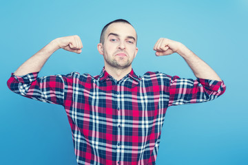 Portrait of a strong male, narcissistic young man shows his strength, front view, blue background, toned