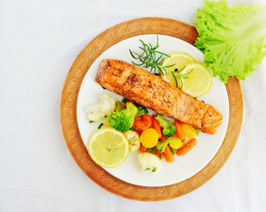 Salmon steak with vegetables, lemon and rosemary over white plate, top view, overhead.