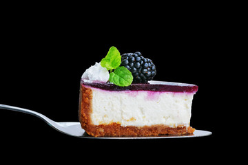 Blackberry cheesecake slice on cake cutter isolated on black. No-bake cheesecake with graham cracker crust, cream cheese filling and blackberry jelly, decorated with whipped cream.