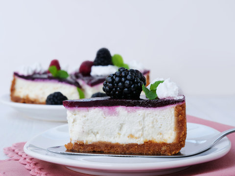 No-bake blackberry cheesecake slice with graham cracker crust, cream cheese filling and blackberry jelly, decorated with whipped cream on cake cutter over white plate.