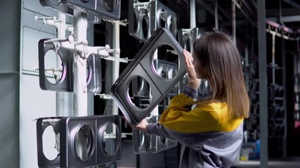 A young pretty white woman works in the paint shop of the plant, she checks the unpainted metall products and making record in check list.